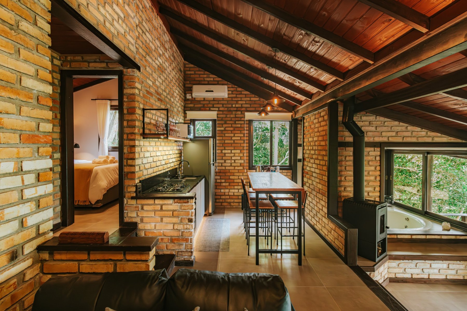 Sala da Cabana Odoyá com madeira, tijolos e janelas para a vegetação